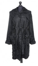 Load image into Gallery viewer, Black knee-length astrakhan coat with a tie, pockets at front, and fur hooks fastening. Lined inside with a deep vent at the back.