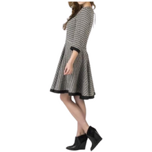 Load image into Gallery viewer, A woman wearing a knee-length checkered linen dress with a fitted waist and flared skirt, paired with black ankle boots.