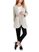 Load image into Gallery viewer, A woman wearing a beige linen cardigan with deep light front pockets, textile belt, paired with black pants and black shoes.
