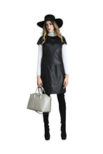 Load image into Gallery viewer, Woman wearing a black leather dress, white shirt, black hat, and black boots holding a beige handbag on a white background.