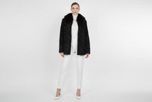 Įkelti nuotrauką į galerijos peržiūros programą, A model stands against a light gray studio background wearing a black textured faux-fur jacket with a wide collar, a white turtleneck, white trousers, and white pointed heels.
