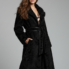 Įkelti nuotrauką į galerijos peržiūros programą, A woman modeling a long black textured faux-fur coat with a matching belt, paired with black pants and tall black boots, against a solid gray studio background.

