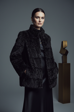 Įkelti nuotrauką į galerijos peržiūros programą, A model wearing a black textured faux-fur jacket over a black satin dress, standing in front of a dark gray studio background next to a gold abstract sculpture.
