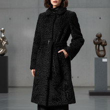 Įkelti nuotrauką į galerijos peržiūros programą, A woman models a long black textured coat with an abstract tonal pattern, paired with a black skirt and black ankle boots, standing in a minimalist gray gallery space with abstract sculptures.
