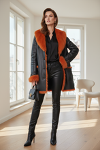 Įkelti nuotrauką į galerijos peržiūros programą, A woman stands in a bright room wearing a black faux-leather coat with a bold burnt orange fur collar and lining, paired with black leather pants and black heeled boots. She holds a small black handbag.
