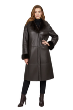 Load image into Gallery viewer, A woman models a dark brown faux-leather coat with a thick dark brown fur collar and cuffs, paired with black pants and brown ankle boots, against a light gray studio background.
