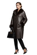 A woman models a dark brown leather coat with a luxurious dark brown fur collar, paired with black trousers, black gloves, and a black crocodile-embossed handbag with gold hardware, set against a solid gray studio background.