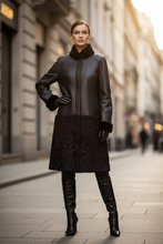 Load image into Gallery viewer, A woman stands on a city street wearing a black faux-leather coat with a high black fur collar, black gloves, black leather knee-high boots, and a textured black skirt.
