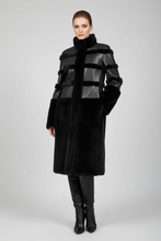 Įkelti nuotrauką į galerijos peržiūros programą, A model wearing a long black coat with mixed textures, including faux leather horizontal bands and a high collar, paired with black leather boots, against a light gray studio background.

