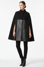 Load image into Gallery viewer, A model wearing a black cape-style coat with a wide black collar and a contrasting black faux-leather front panel, paired with black pants and black ankle boots, against a plain white studio background.
