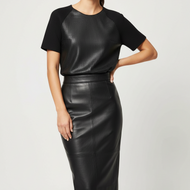 A woman modeling a black short-sleeve top with textured raglan sleeves and a black faux-leather pencil skirt, photographed against a light gray studio background.