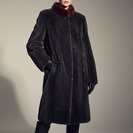 A model wears a dark charcoal gray textured coat with a contrasting dark brown fur collar, paired with black leather gloves and black leather knee-high boots, set against a plain gray studio background.