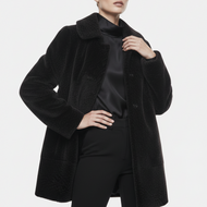 A model wearing a black textured teddy coat over a black satin top and black pants, photographed against a clean light gray studio background.