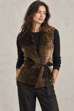 Įkelti nuotrauką į galerijos peržiūros programą, A woman modeling a brown faux fur wrap vest with a black ribbon tie belt, worn over a black long-sleeve top and black pants, against a neutral beige background.
