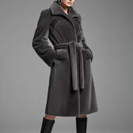 A model wears a dark gray plush faux fur coat with a matching waist belt, paired with black knee-high boots, against a neutral gray studio background.