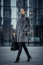 Įkelti nuotrauką į galerijos peržiūros programą, A woman walks outdoors in front of a modern glass building, wearing a gray faux-fur coat with a textured lower panel, black leather pants, black high-heeled boots, and carrying a black handbag.
