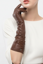 Įkelti nuotrauką į galerijos peržiūros programą, A close-up of a model wearing a long, elegant brown leather glove with ruched detailing and a small metal logo button near the cuff, paired with a white top against a clean white background.
