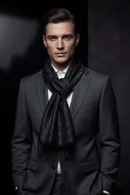 Įkelti nuotrauką į galerijos peržiūros programą, A man in a dark gray suit and white dress shirt wearing a black patterned scarf with fringe, posed against a dark studio background.
