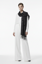 Įkelti nuotrauką į galerijos peržiūros programą, A model wearing a white long-sleeve jumpsuit and a black patterned fringed scarf, standing against a seamless white studio background.

