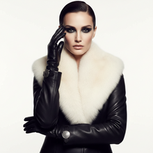 Load image into Gallery viewer, A model wearing a black leather jacket with a large white fur collar, black leather gloves, and dramatic black eye makeup, posing against a solid white background.
