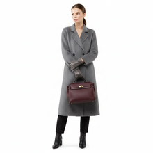 Įkelti nuotrauką į galerijos peržiūros programą, A model wearing a long gray double-breasted coat, dark leather gloves, black trousers, and black ankle boots, holding a burgundy leather handbag with gold hardware against a plain white background.
