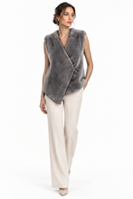 Load image into Gallery viewer, A woman modeling a sleeveless gray faux fur wrap vest over cream wide-leg trousers, photographed against a seamless white studio background.
