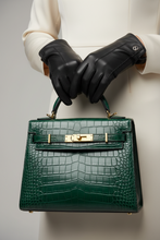 Įkelti nuotrauką į galerijos peržiūros programą, A structured green crocodile-embossed handbag with gold-tone hardware, held by a person wearing black gloves and a cream-colored blazer against a neutral studio background.

