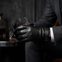 Load image into Gallery viewer, A person in a dark gray suit holding a glass of whiskey, wearing a black leather glove on one hand. The background is a dark, moody bar or studio setting with a bottle and glasses.
