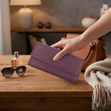 Įkelti nuotrauką į galerijos peržiūros programą, Hand holding a purple wallet on a wooden surface with sunglasses and a handbag in the background.
