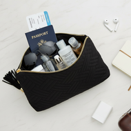 Black travel pouch with travel items on a white surface