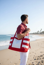 Load image into Gallery viewer, Man carrying a red and white striped bag on a beach

