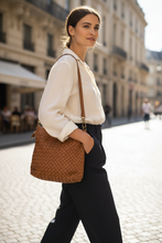 Įkelti nuotrauką į galerijos peržiūros programą, A woman in a white blouse and black trousers walks on a cobblestone street while carrying a brown woven shoulder bag.
