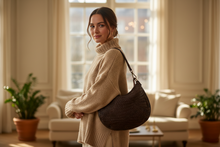 Load image into Gallery viewer, Woman in a beige sweater holding a brown handbag in a living room.
