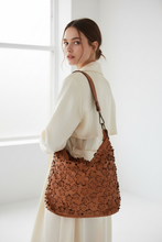 Įkelti nuotrauką į galerijos peržiūros programą, A woman in a cream dress carries a large brown leather shoulder bag with an allover floral cutout pattern, photographed in a bright, minimalist room.
