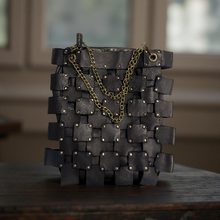 Load image into Gallery viewer, Black woven leather bag with gold chain on a wooden surface
