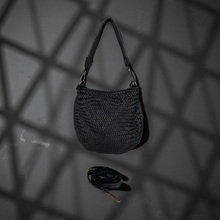 Load image into Gallery viewer, Black woven handbag on a dark textured surface with geometric shadows
