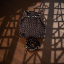 Load image into Gallery viewer, Brown woven bag with a strap on a wooden surface with shadow patterns
