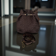 Load image into Gallery viewer, Brown woven handbag with a strap on a reflective surface
