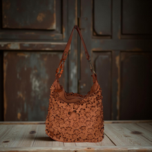 Load image into Gallery viewer, Brown leather handbag with floral patterns on a wooden surface and rustic background
