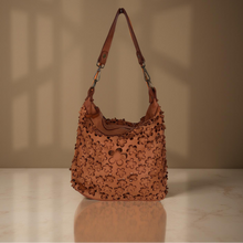 Load image into Gallery viewer, Brown leather handbag with floral patterns on a beige surface and background
