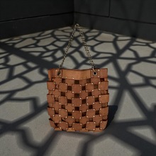 Load image into Gallery viewer, Brown woven handbag with chain handle on a gray surface with geometric shadow pattern
