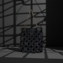 Load image into Gallery viewer, Black woven handbag with chain strap on a dark background

