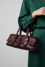 Įkelti nuotrauką į galerijos peržiūros programą, A dark burgundy leather handbag with braided shoulder straps and silver-tone buckle details, carried by a model wearing a matching dark green satin dress against a light gray studio background.

