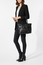 Įkelti nuotrauką į galerijos peržiūros programą, A woman models a black leather shoulder tote bag with silver-tone hardware, styled with a black blazer, white top, black skinny pants, and black ankle boots against a clean white studio background.
