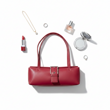 Įkelti nuotrauką į galerijos peržiūros programą, A structured red leather handbag is arranged on a white background with surrounding beauty and jewelry props, including a lipstick, rings, a necklace, a perfume bottle, and a compact mirror.
