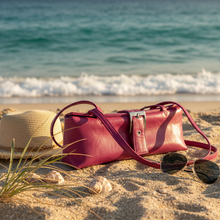 Load image into Gallery viewer, Red handbag, straw hat, and sunglasses on a sandy beach with ocean waves in the background
