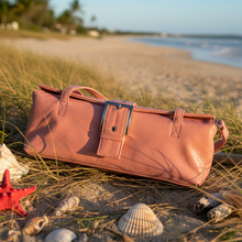 Load image into Gallery viewer, Brown leather bag on a sandy beach with grass and shells around
