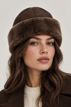 Įkelti nuotrauką į galerijos peržiūros programą, A close-up portrait of a woman wearing a brown fur-trimmed aviator-style hat and a cream knit sweater against a light gray studio background.
