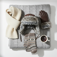 Winter accessories including a scarf, hat, gloves, and socks on a textured surface with a cup of coffee.