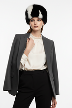 Įkelti nuotrauką į galerijos peržiūros programą, A model wearing a black and white fur ushanka hat, a gray blazer, a cream satin blouse, and black trousers, posed against a solid white studio background.
